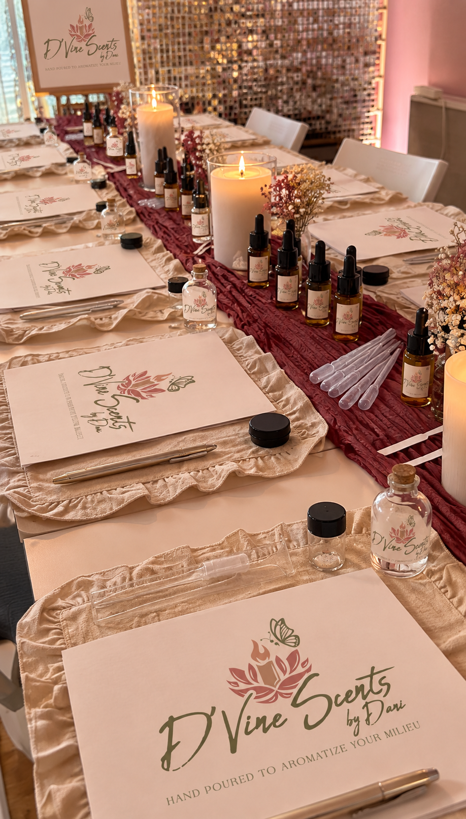 A candle-making party table set with place settings, branded booklets, and lit pillar candles